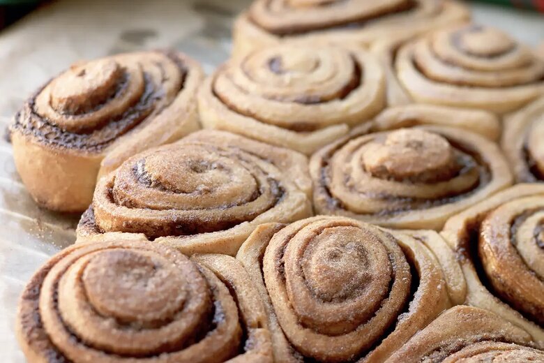 A close-up of freshly baked cinnamon swirls arranged in a glass baking dish, with a festive red and green striped cloth in the background, perfect for the 12 days of Christmas.