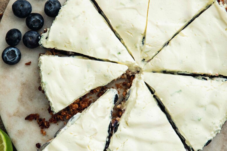 A blueberry cheesecake cut into slices on a marble plate, garnished with blueberries and lime slices.