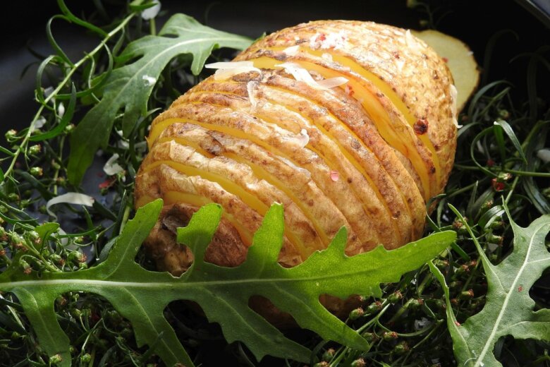 A hasselback potato on a bed of salad leaves