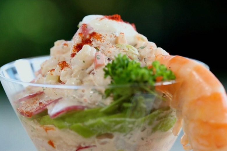 A prawn cocktail served in a glass dish with a prawn placed on the edge pointing down.