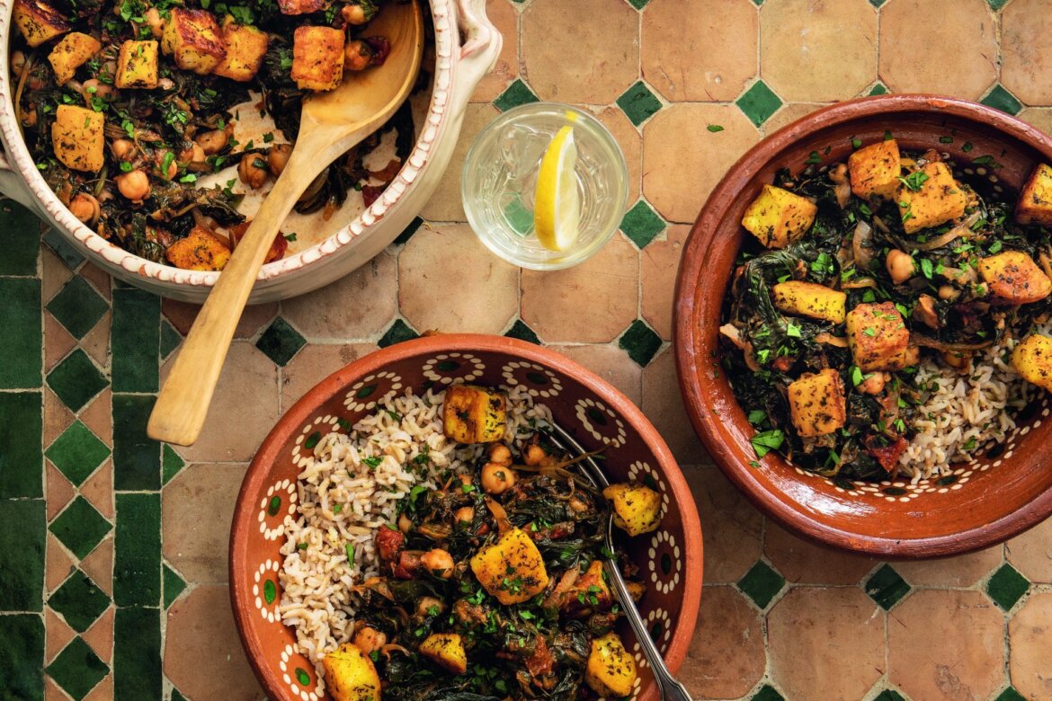 Traditional dishes with halloumi, spinach, and brown rice served in clay pots and bowls on a tiled table, accompanied by slices of lemon.