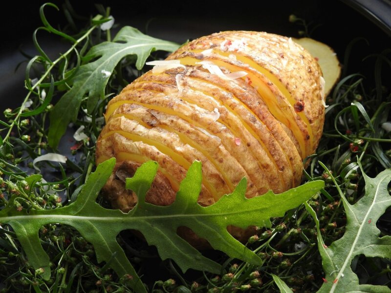 A hasselback potato on a bed of salad leaves