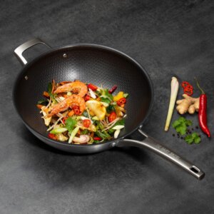 A HexGuard wok pan with a vegetable stir-fry and prawns on a black surface.